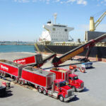 Two red trucks in front of vessel on wharf